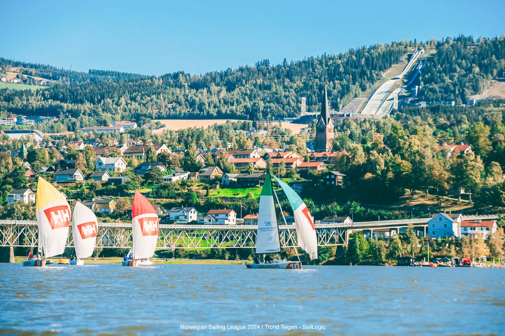 Da Lillehammer fikk Seilsportsligaen på besøk ble det seilt med historiske og spektakulære kulisser i bakgrunnen, her Lysgårds-bakkene, som var gjenstand for hoppkonkurransene og åpningsseremoniene under vinter-OL i 1994. (Foto: Trond Teigen, SailLogic)